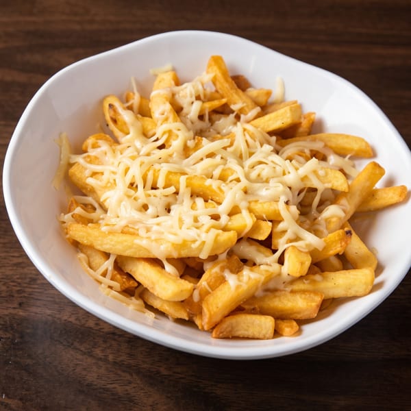 A white bowl filled with golden french fries topped with melted shredded cheese on a wooden table.